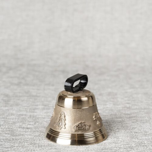 Petite cloche métallique dorée décorée de motifs en relief (arbres, maisons, paysages) et d'une anse noire, posée sur un tissu gris clair texturé.